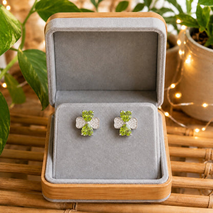 Silver crystal bow stud earrings featuring peridot green heart-cut stones displayed in a premium grey velvet jewellery box.
