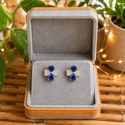Silver crystal bow stud earrings featuring royal blue heart-cut stones displayed in a premium grey velvet jewellery box.