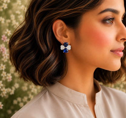 Model wearing silver crystal bow stud earrings with royal blue heart-cut crystals.