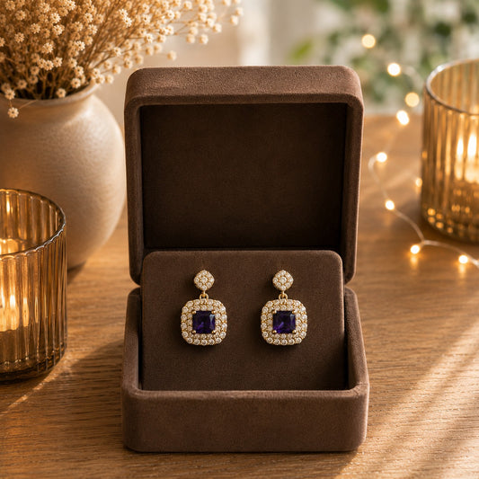 Gold halo square drop earrings with royal purple princess-cut crystals displayed in a premium mocha velvet jewellery box.