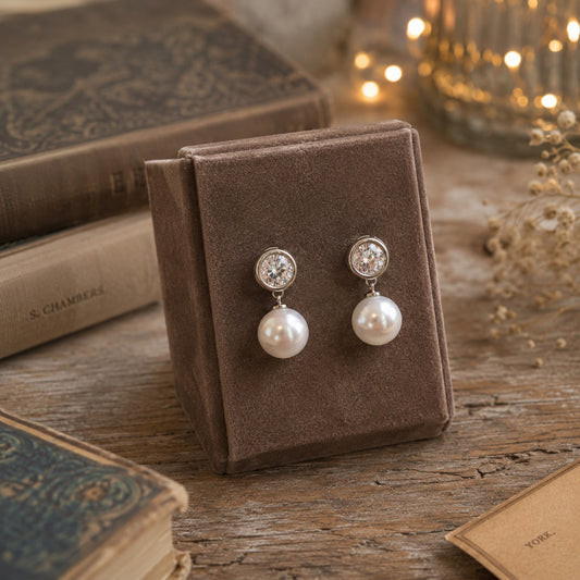 Classic silver pearl drop stud earrings with crystal studs displayed on a premium mocha velvet jewellery stand in a luxury styled setting.