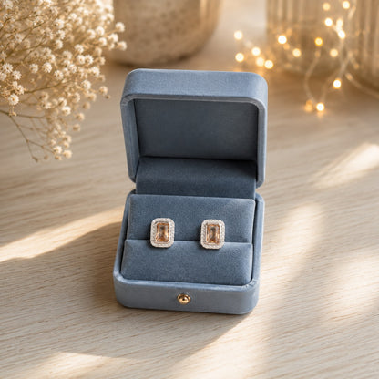 Champagne emerald-cut halo stud earrings displayed in a premium blue velvet jewellery box