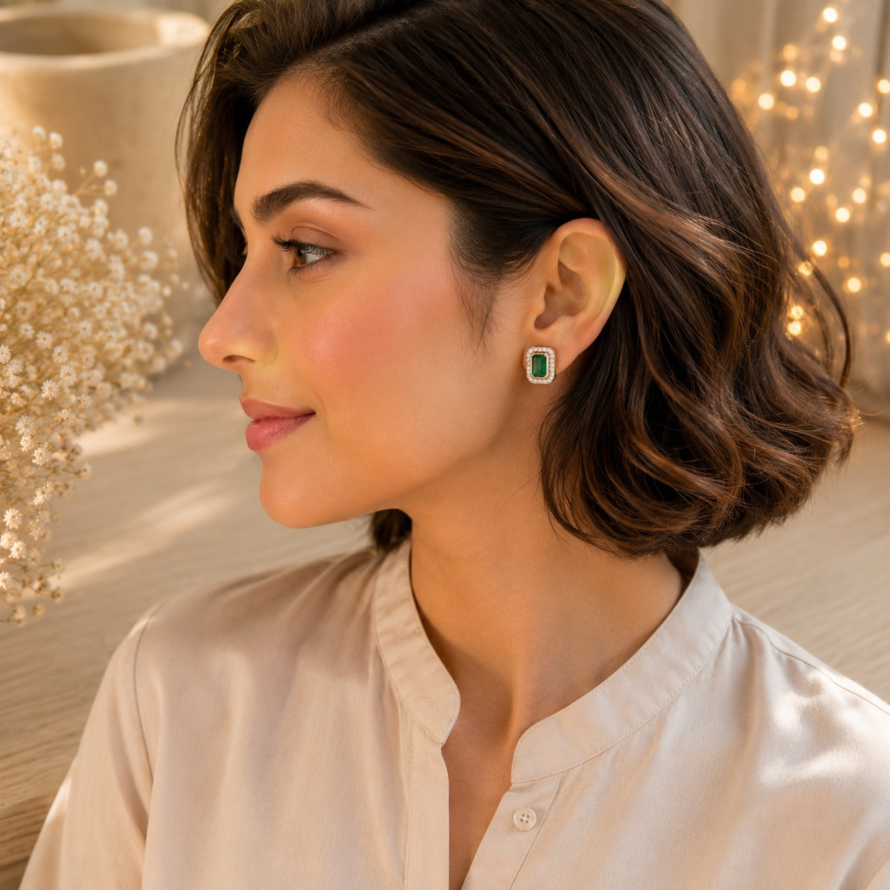 Woman wearing emerald green emerald-cut halo stud earrings in silver finish, premium gemstone jewellery close-up
