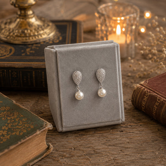 Silver pavé crystal teardrop pearl drop earrings displayed on a premium velvet jewelry stand in an elegant luxury styling setting.