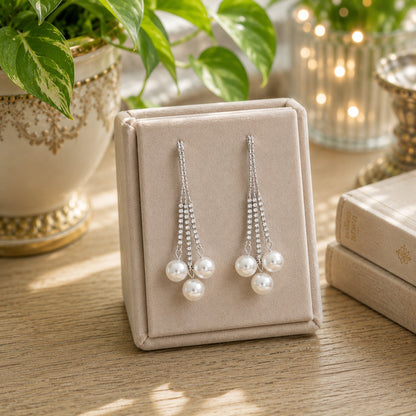 Silver crystal tassel earrings with three pearl drops displayed on a premium velvet jewelry stand in a luxury boutique setting