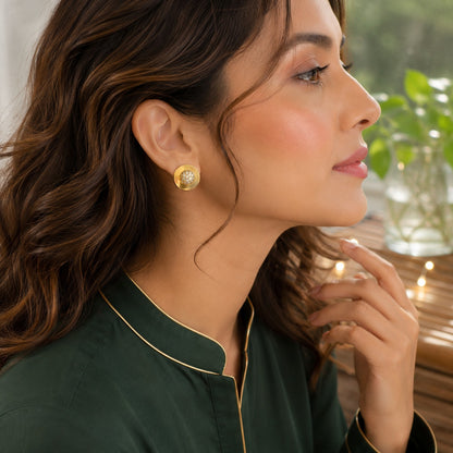 Model wearing gold round crystal disc stud earrings in a polished metal finish with a side-profile portrait in natural daylight