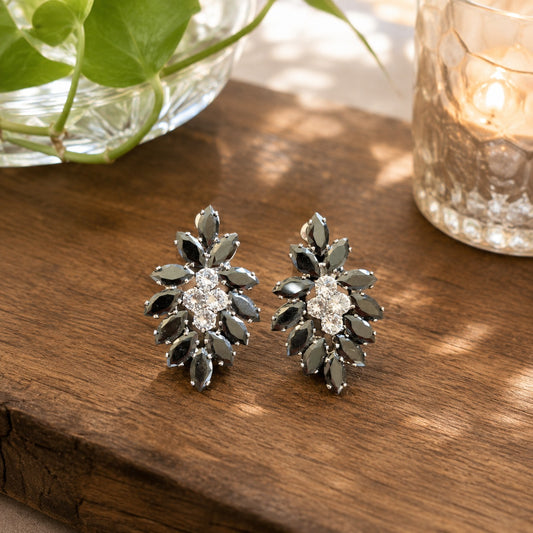 Pair of black crystal floral statement earrings with a brilliant clear crystal center displayed on a natural wooden surface in soft daylight.