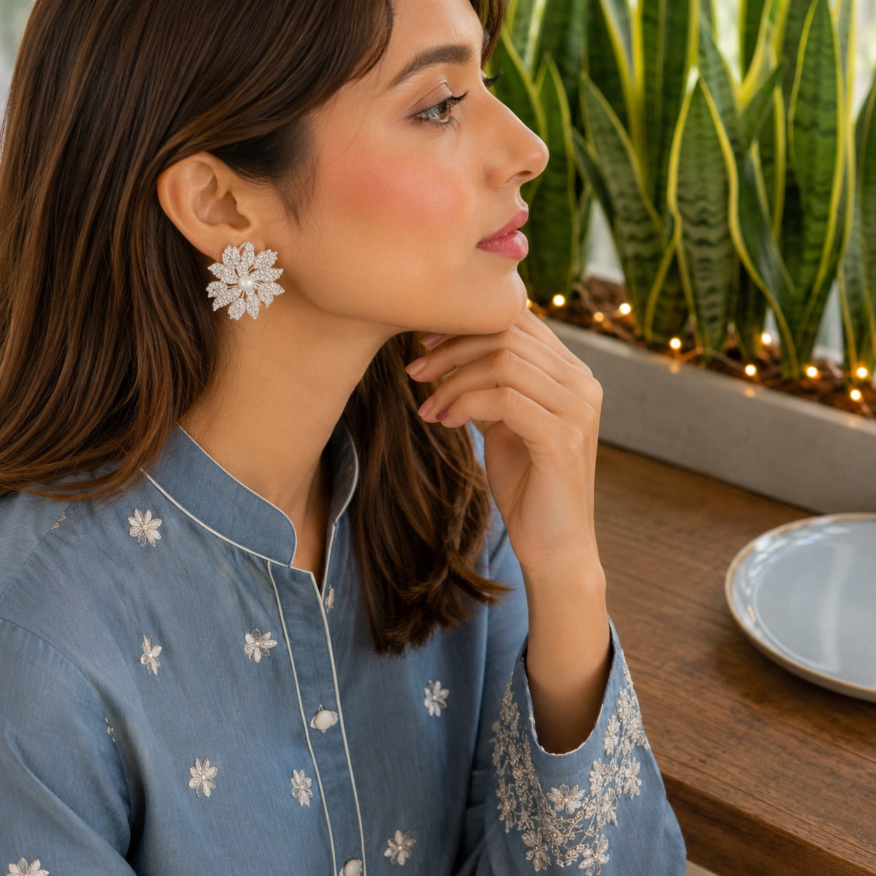 Model wearing silver crystal floral pearl stud earrings with sparkling pavé petals and a pearl center in a side-profile lifestyle portrait.