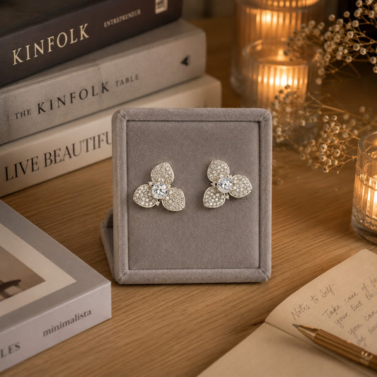 Pair of silver crystal floral stud earrings with pavé crystal petals and a brilliant center stone displayed on a premium grey velvet jewelry stand.