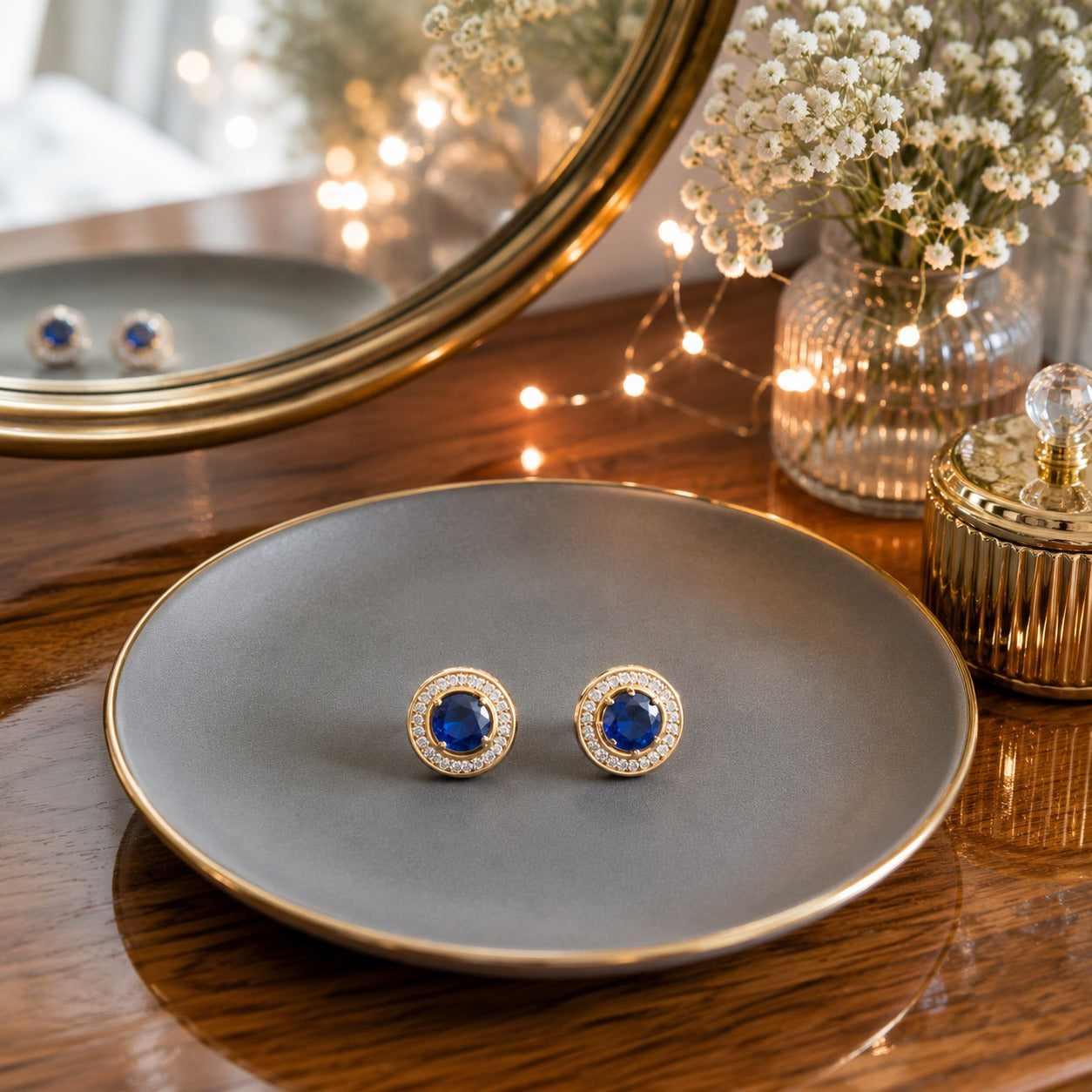 Round halo blue gemstone stud earrings displayed on a matte grey ceramic plate with a luxury vanity setting.