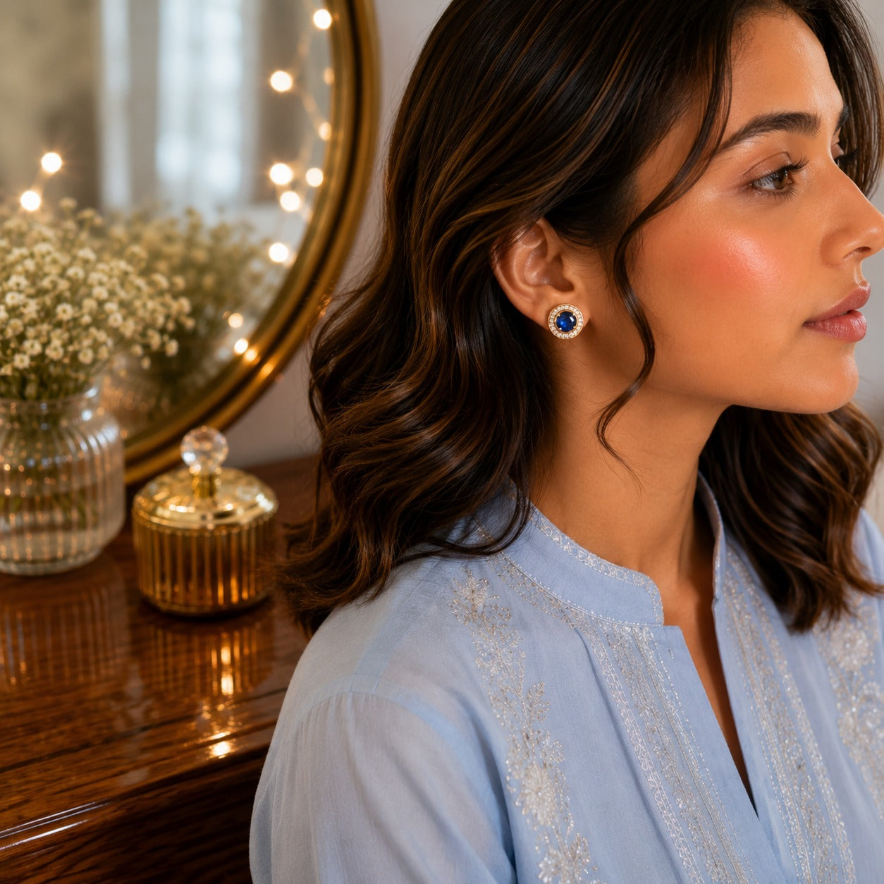 Woman wearing blue round halo gemstone stud earrings in a side-profile portrait with a premium dressing table background.