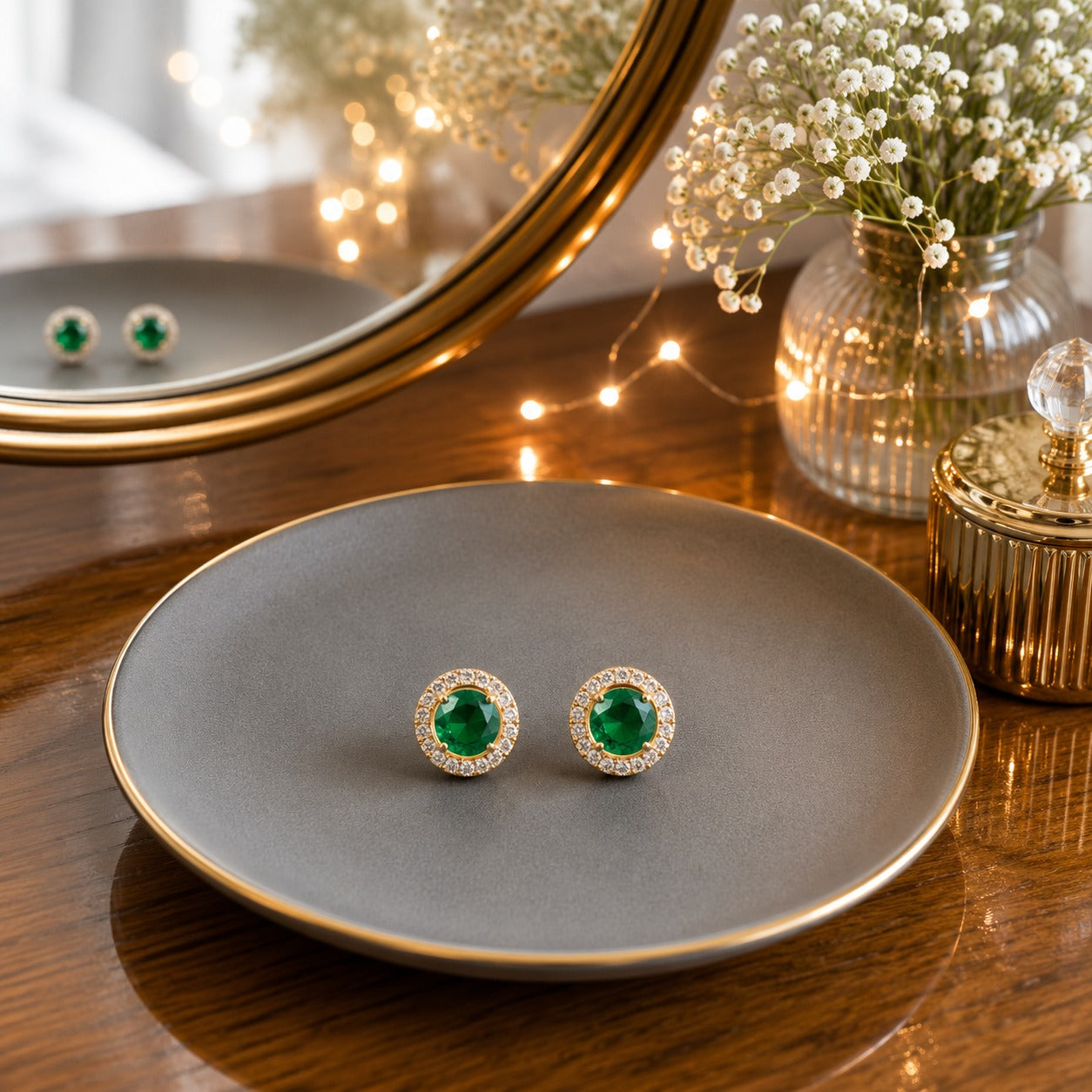 Round halo green gemstone stud earrings displayed on a matte grey ceramic plate with a luxury vanity setting.