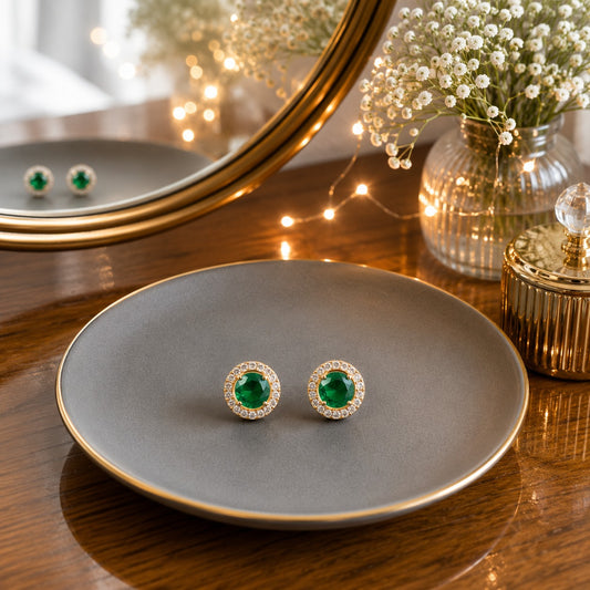 Round halo green gemstone stud earrings displayed on a matte grey ceramic plate with a luxury vanity setting.