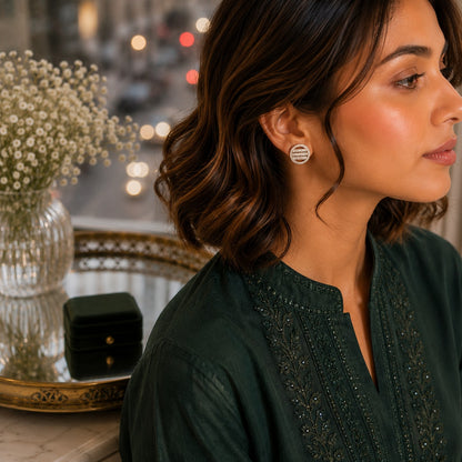 Woman wearing round geometric crystal disc stud earrings with a dark green embroidered outfit in a luxury indoor setting.