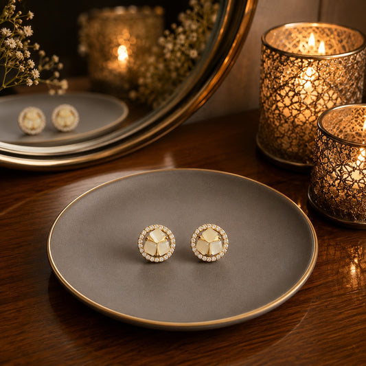 Round Mother of Pearl halo stud earrings displayed on a matte grey ceramic plate with warm candlelight and a premium dressing table background