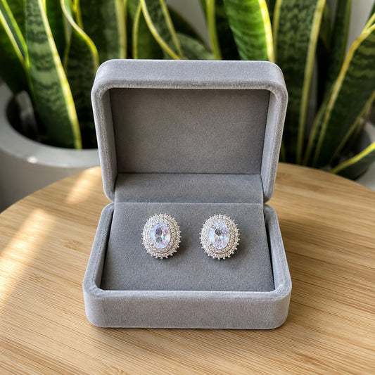 Silver-tone oval halo crystal stud earrings displayed in a premium light grey velvet jewellery box on a bamboo wooden table