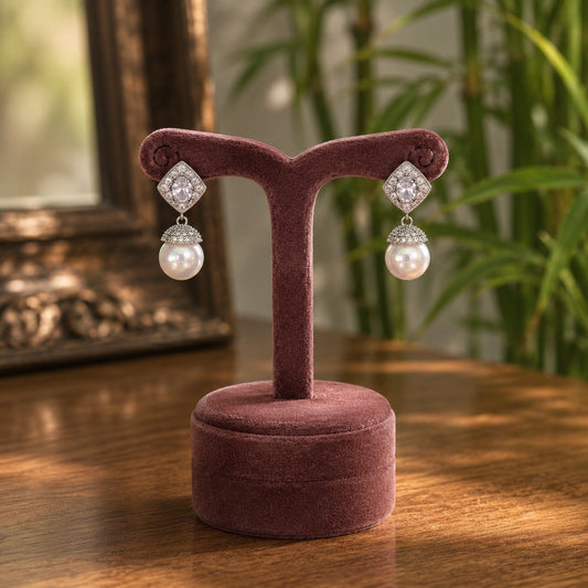 Woman wearing silver crystal and pearl drop earrings with a mauve outfit in a bright luxury indoor setting.