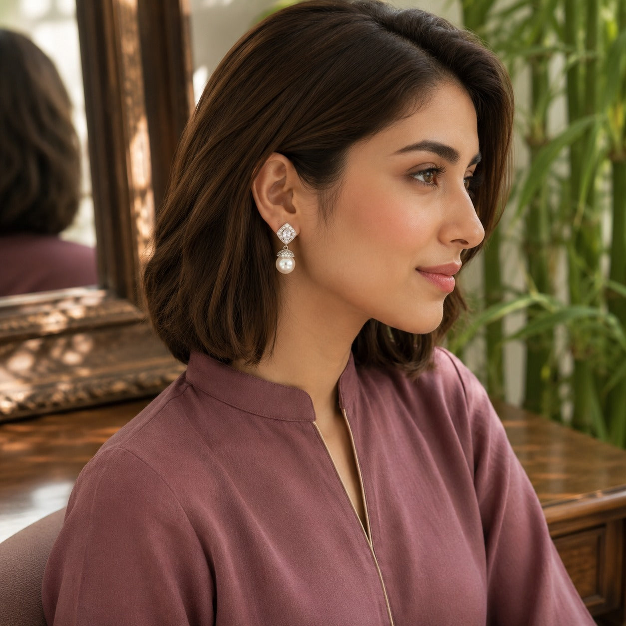 Silver crystal and pearl drop earrings displayed on a premium mauve velvet jewellery stand with a softly blurred luxury interior background.