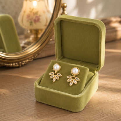 Pearl and marquise gold crystal drop earrings displayed in a premium olive green velvet jewellery box on a wooden dressing table.