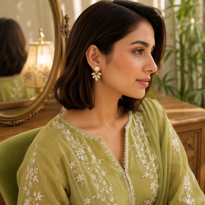 Woman wearing pearl and marquise  gold crystal drop earrings with a light olive embroidered outfit in a bright luxury indoor setting.