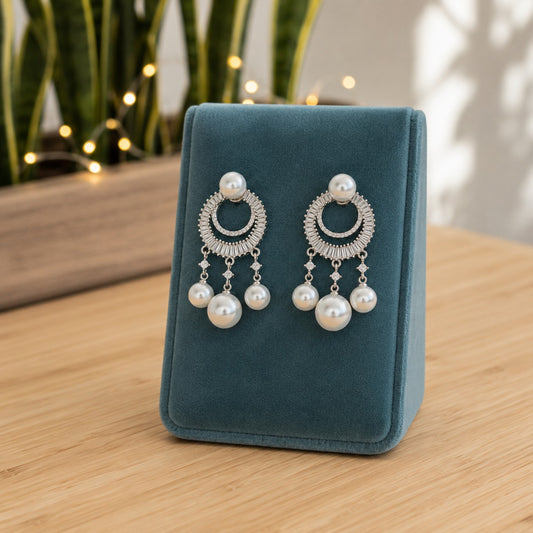 Silver pearl crystal chandelier drop earrings displayed on a premium blue velvet jewellery stand with a softly blurred indoor background.