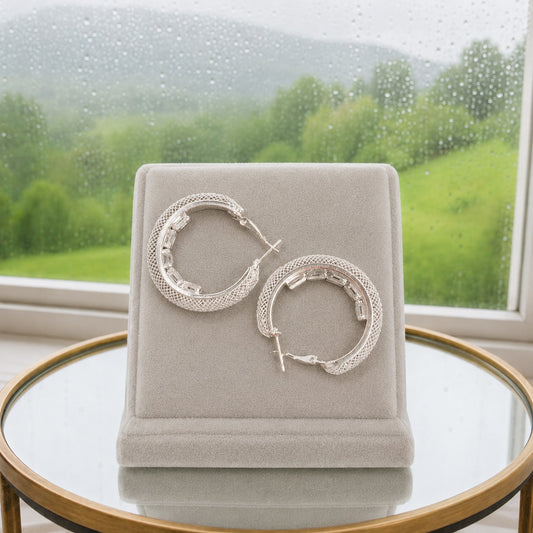 Rear view of silver textured hoop earrings showing the secure hinged snap-lock clasp and textured crystal finish on a luxury velvet display stand.