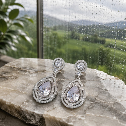 Premium silver teardrop crystal drop earrings with pear-cut centre crystal displayed on a natural marble slab in soft daylight, luxury jewellery product photography.