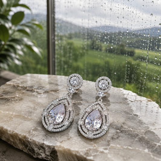 Premium silver teardrop crystal drop earrings with pear-cut centre crystal displayed on a natural marble slab in soft daylight, luxury jewellery product photography.