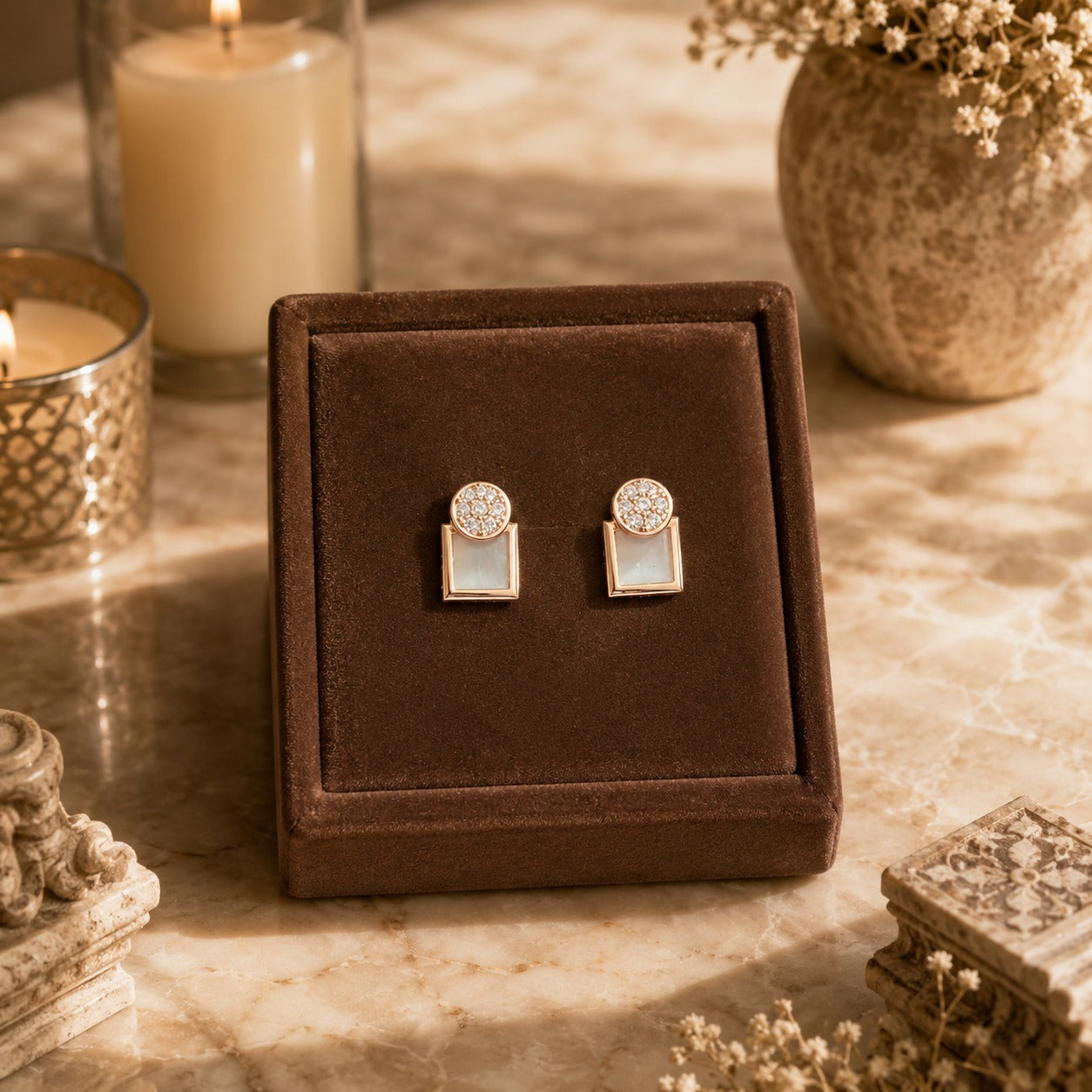 Gold geometric mother of pearl zircon stud earrings displayed on a premium brown velvet jewellery stand with luxury candle-lit décor and marble background.