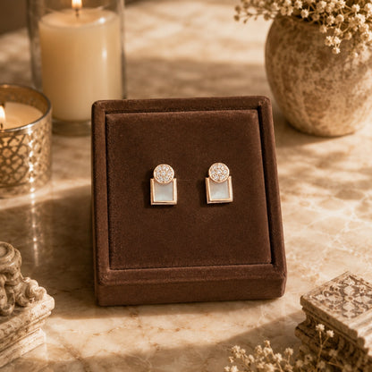 Gold geometric mother of pearl zircon stud earrings displayed on a premium brown velvet jewellery stand with luxury candle-lit décor and marble background.