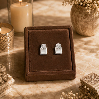 Silver geometric mother of pearl zircon stud earrings displayed on a premium brown velvet jewellery stand with luxury candle-lit décor and marble background.