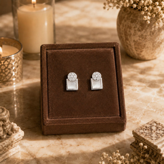 Silver geometric mother of pearl zircon stud earrings displayed on a premium brown velvet jewellery stand with luxury candle-lit décor and marble background.