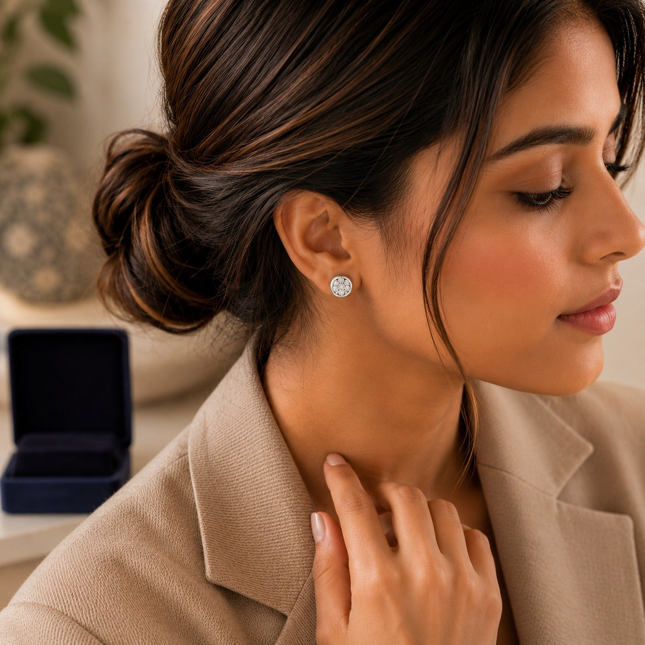 Woman wearing gold floral crystal stud earrings in a side-profile portrait with a neutral beige outfit.