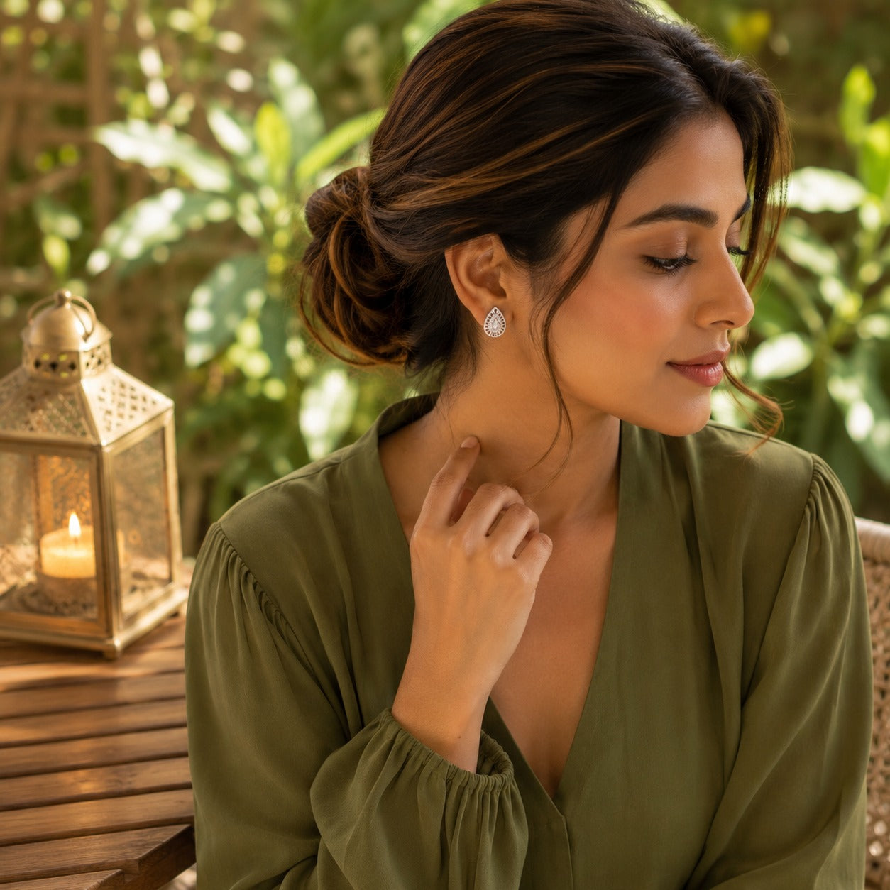 Woman wearing silver teardrop crystal stud earrings with an olive green V-neck blouse in a side-profile outdoor portrait.