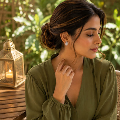 Woman wearing silver teardrop crystal stud earrings with an olive green V-neck blouse in a side-profile outdoor portrait.