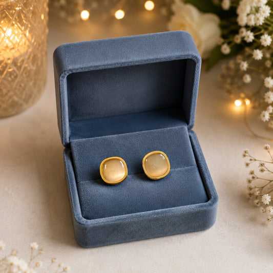 Gold-tone square moonstone stud earrings displayed inside a premium smoky blue velvet jewelry box with a luxury floral background