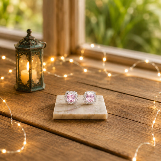 Halo cushion-cut crystal stud earrings with  a soft pink centre stone displayed on a marble slab with warm decorative lighting and a luxury wooden background.