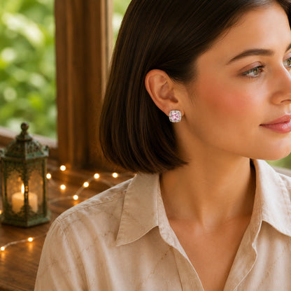 Woman wearing halo cushion-cut crystal stud earrings with a soft pink centre stone in a warm natural daylight setting