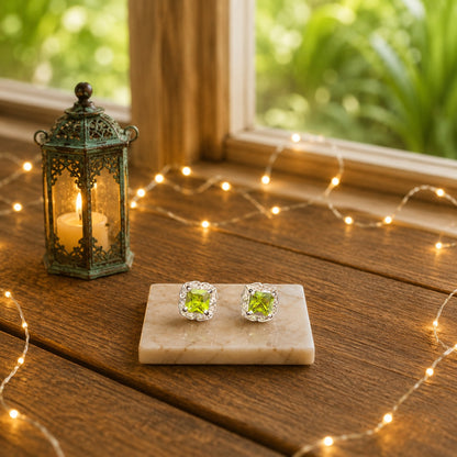 Halo cushion-cut crystal stud earrings with a lime green centre stone displayed on a marble slab with warm decorative lighting and a luxury wooden background.