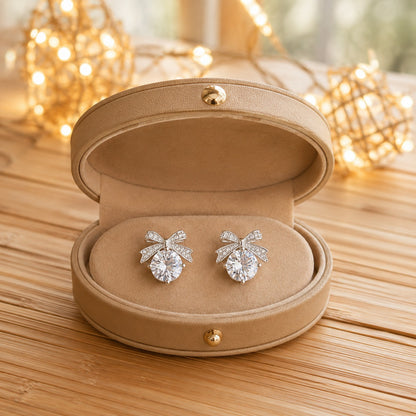 Silver bow stud earrings featuring clear zircon cabochons displayed on a premium black mirrored jewellery tray.