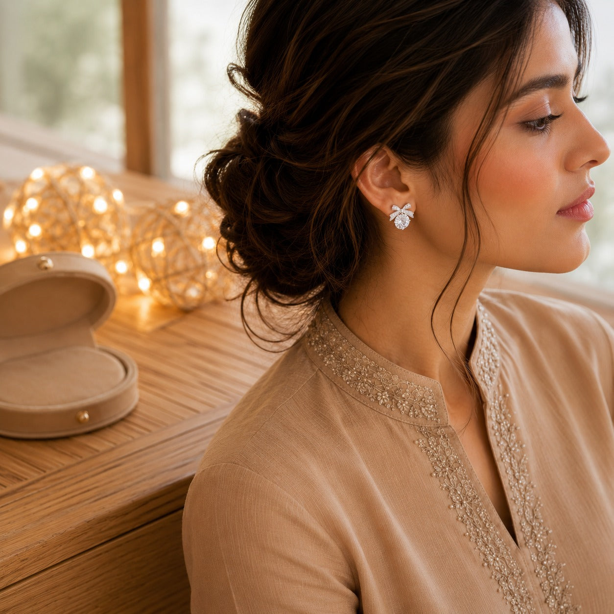 Woman wearing silver bow stud earrings with luminous Mother of zircon stones in a luxury indoor setting.