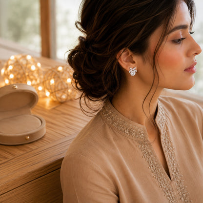 Woman wearing silver bow stud earrings with luminous Mother of zircon stones in a luxury indoor setting.