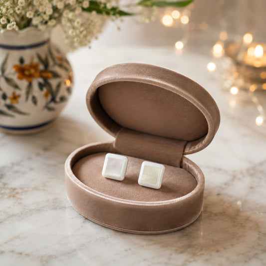 Square mother of pearl stud earrings displayed inside a premium taupe jewellery box on a luxury marble surface.