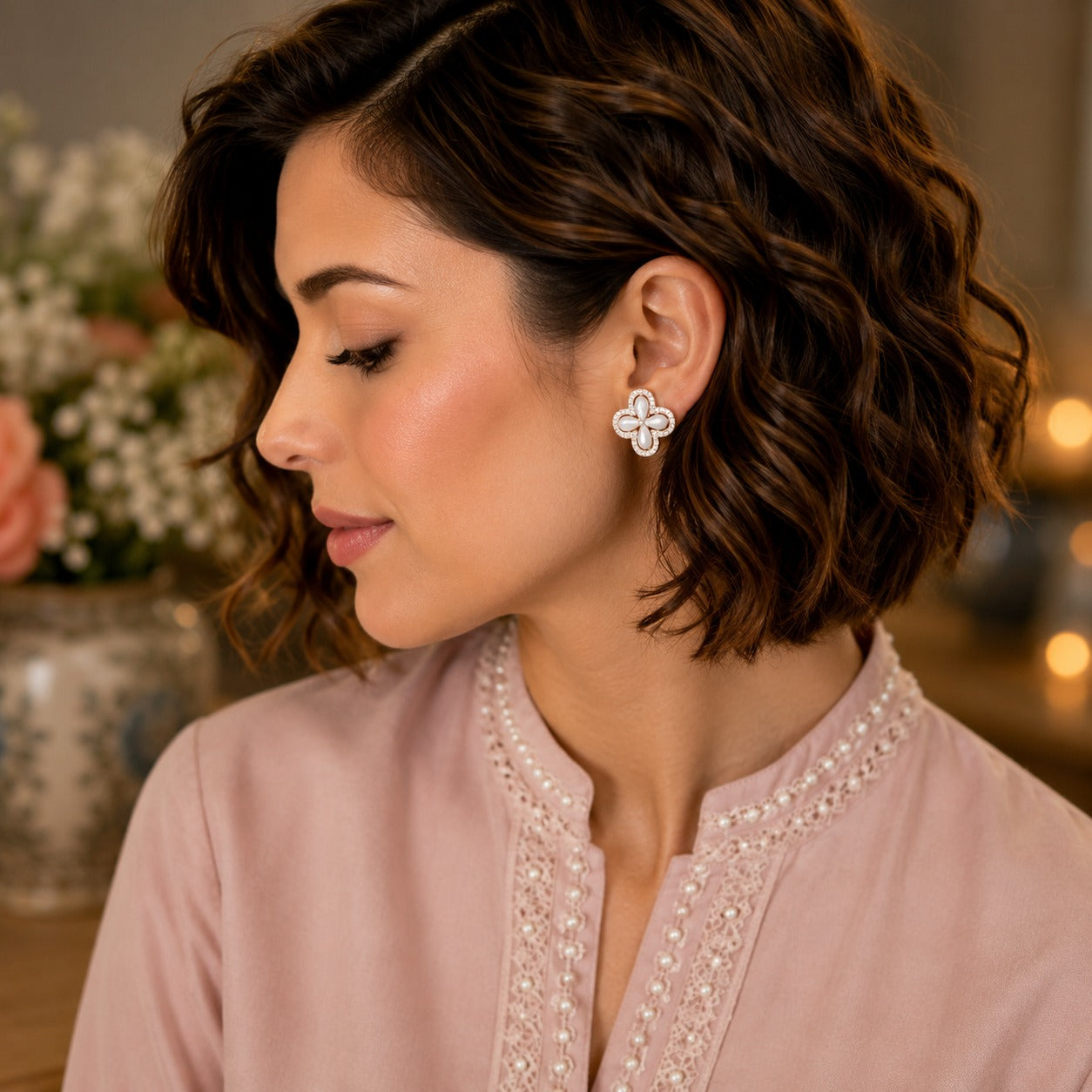 Woman wearing elegant silver-tone mother-of-pearl floral stud earrings in a soft side-profile portrait with a blush pink outfit.