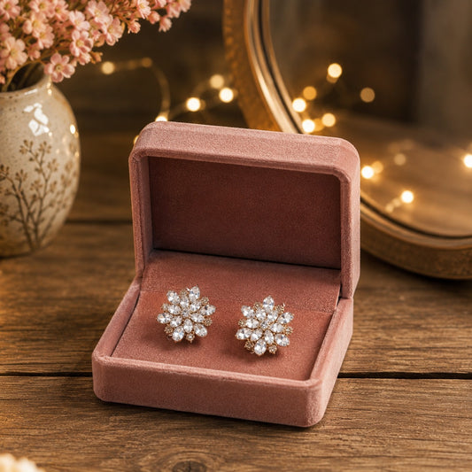 Crystal floral stud earrings displayed inside a premium blush pink velvet jewellery box on a wooden vanity with warm fairy lights and luxury décor background