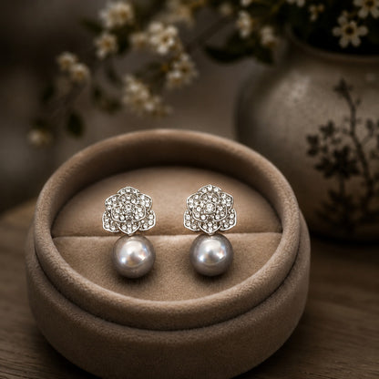 Silver crystal floral stud earrings with lustrous grey pearl drops displayed on a premium taupe velvet jewellery stand with a softly blurred luxury background.