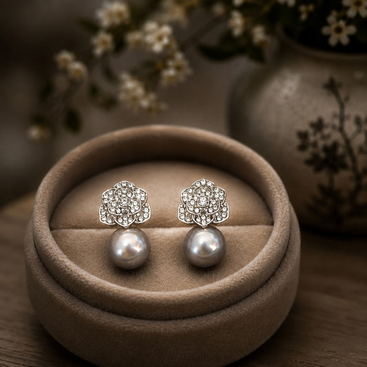 Silver crystal floral stud earrings with lustrous grey pearl drops displayed on a premium taupe velvet jewellery stand with a softly blurred luxury background.