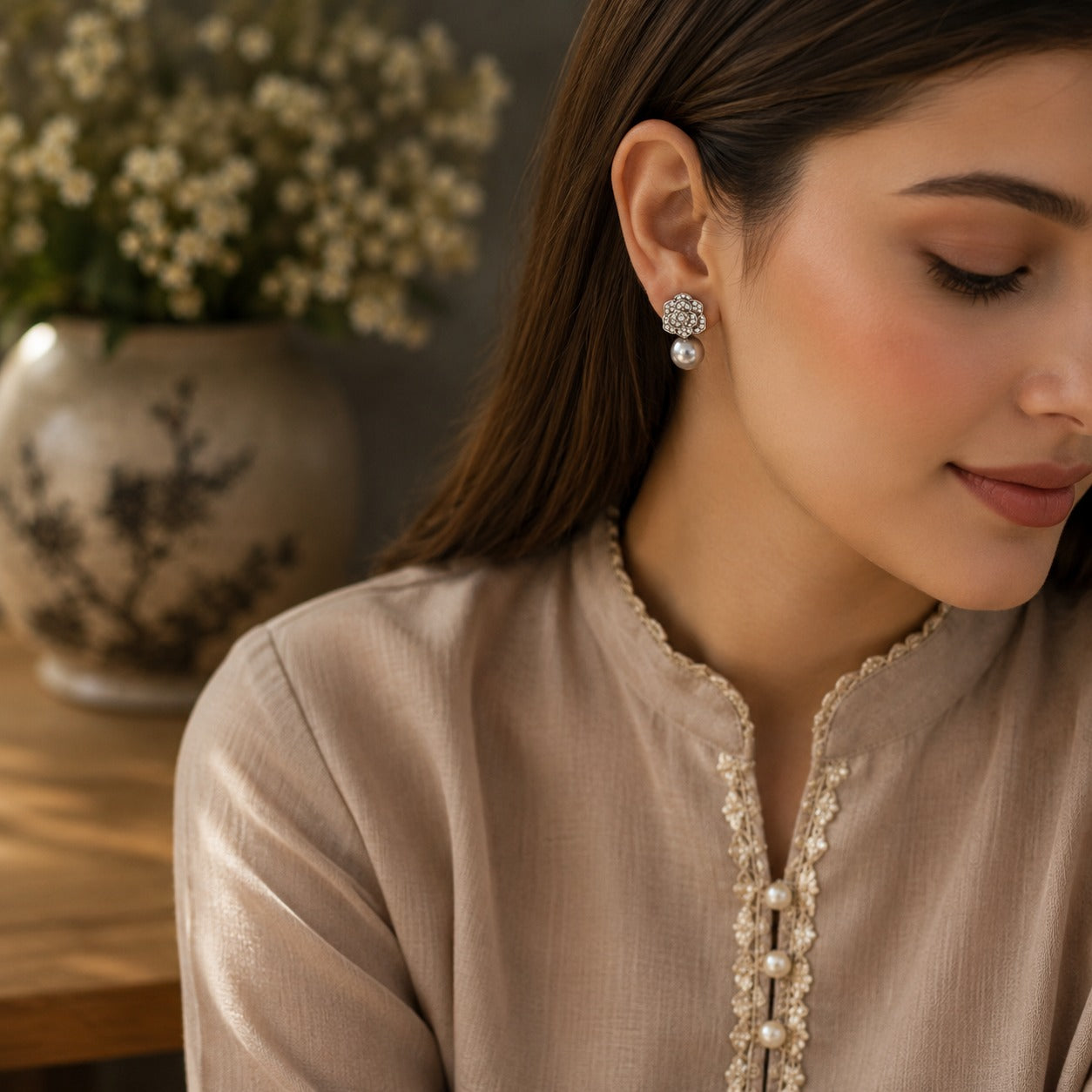 Woman wearing silver crystal floral earrings with a glossy grey pearl drop, styled with a soft taupe outfit in a luxury lifestyle setting