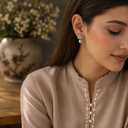 Woman wearing silver crystal floral earrings with a glossy grey pearl drop, styled with a soft taupe outfit in a luxury lifestyle setting