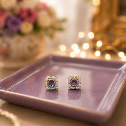 Silver square halo stud earrings featuring round mystic rainbow crystal centre stones displayed on a premium lavender ceramic tray with a softly blurred luxury background.